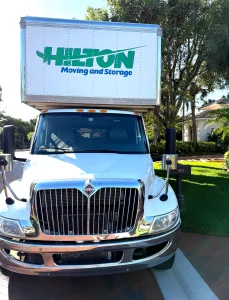Moving truck parked outside a house, labeled &ldquo;Hilton Moving and Storage.&rdquo;