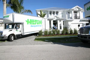 Moving truck parked in front of a large white house with palm trees.